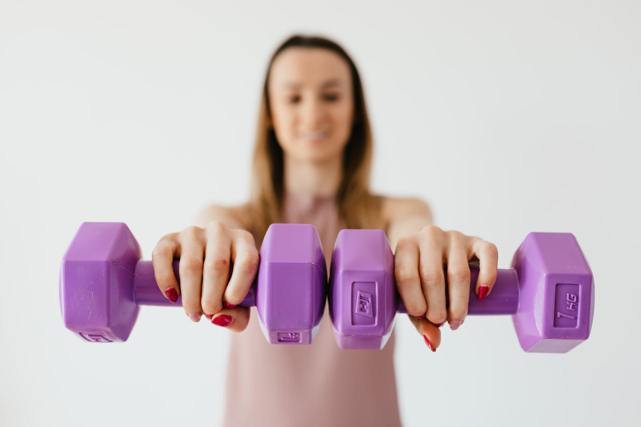 Defocused content young female doing bicep exercise with dumbbells during functional training in light studio