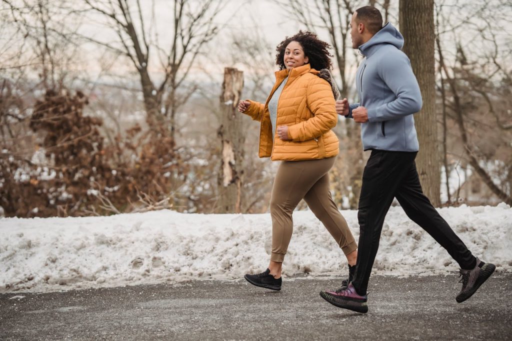 Full body of positive curvy African American woman and black coach looking at each other while jogging on asphalt walkway in winter time