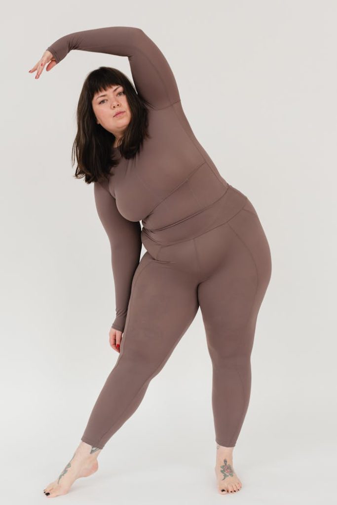 Young plus size woman stretching body in white studio