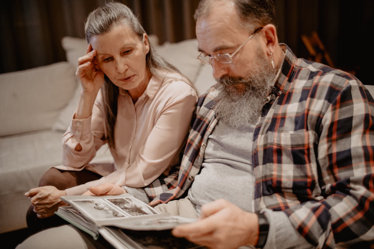 about-05 A senior couple reminisces while looking through a photo album at home, reflecting on cherished memories.