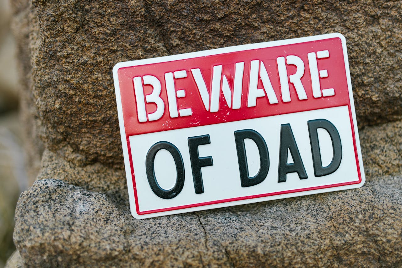 Close-up of a humorous 'Beware of Dad' sign placed against a rocky background, emphasizing parental protection.