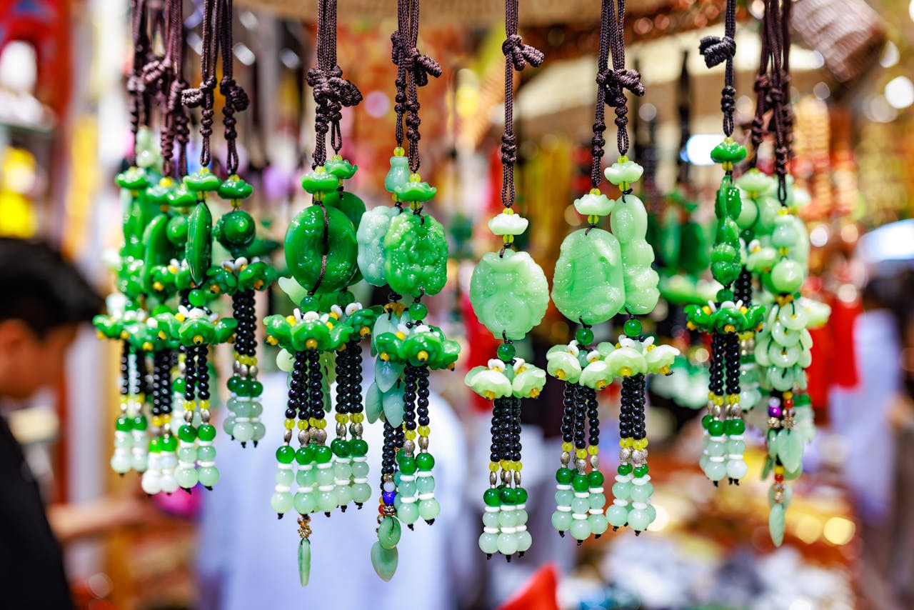 Vibrant green jade ornaments hang in a busy market, showcasing detailed craftsmanship and bright colors.