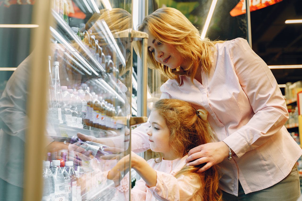 A mother and daughter selecting drinks from a supermarket refrigerator.